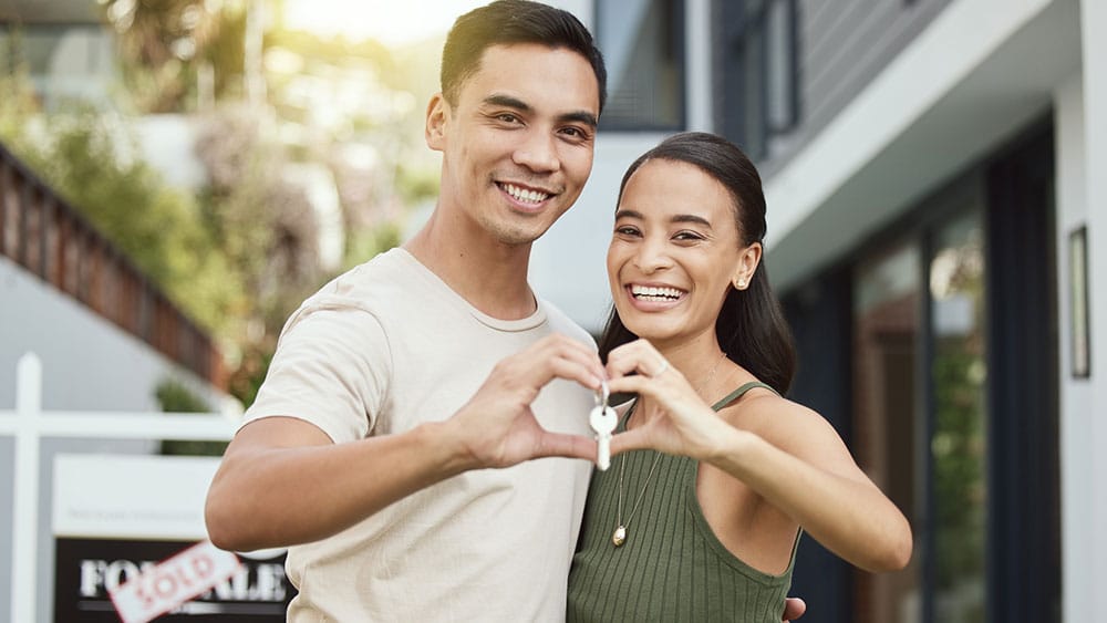 Young couple with keys in front of their new home.