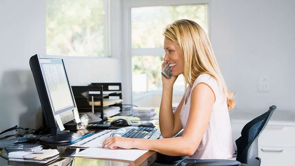 Woman in home office with computer talks to client on phone