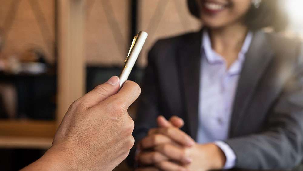 Real Estate agent hands a pen to a client for signing an offer and acceptance form