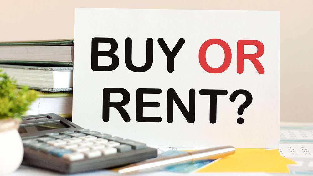 White card with text "buy or rent" stands on the desk against stacked books, calculator, and pen.